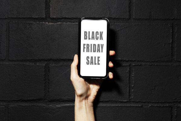 Black Friday sale text on screen of smartphone in female hand. Фон черной кирпичной стены.