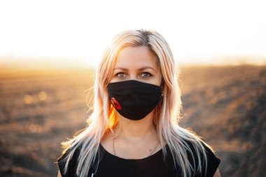 Açık havada, solunum maskesi takan yaşlı bir kadının portresi. Günbatımının arkaplanı.