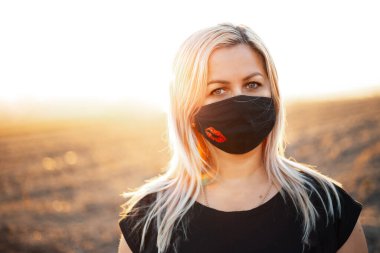 Açık havada, solunum maskesi takan yaşlı bir kadının portresi. Günbatımının arkaplanı.