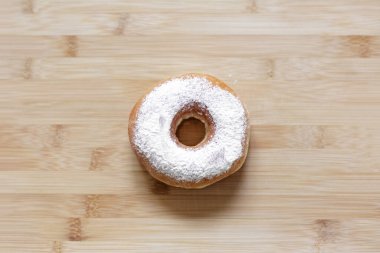 Tahta masanın üzerine beyaz toz serpiştirilmiş donut manzarası.