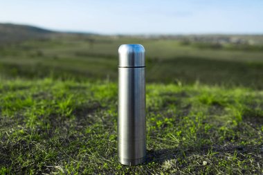 Yeşil çimenlerin üzerindeki çelik paslanmaz termosa yakın çekim.