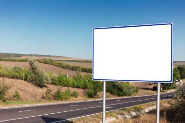 Mavi gökyüzünün arka planındaki asfaltlama yolunun yanındaki reklam afişi için boş ilan panosu.