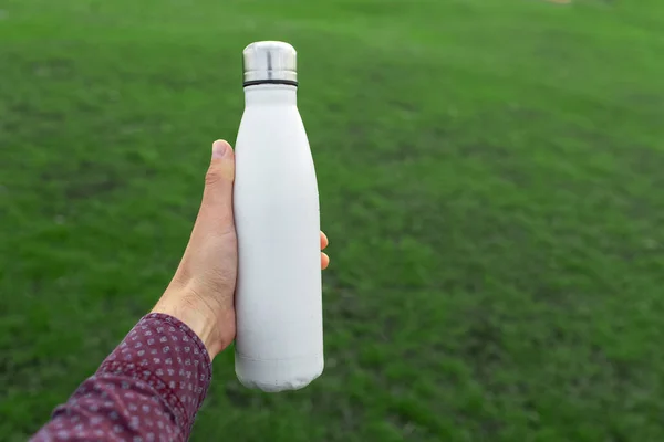 浅谈浅绿色草坪背景下男性手握可重复使用的白色钢制热水瓶的特写 — 图库照片