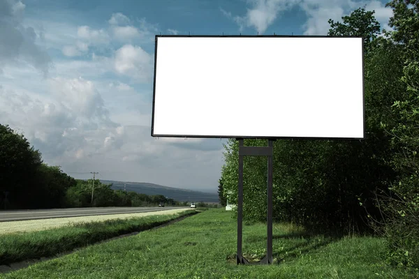 青い空を背景に 舗装道路や緑の森の近くの広告ポスターのための空の看板 — ストック写真