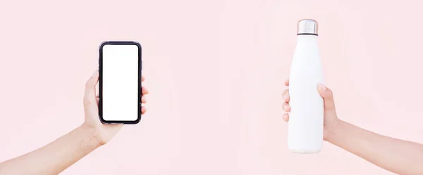Elinde akıllı telefon, elinde maketi ve yeniden kullanılabilir çelik termodinamik beyaz renkli su şişesi var. Pastel pembenin arka planı. Kopya alanı ile panoramik konsept.
