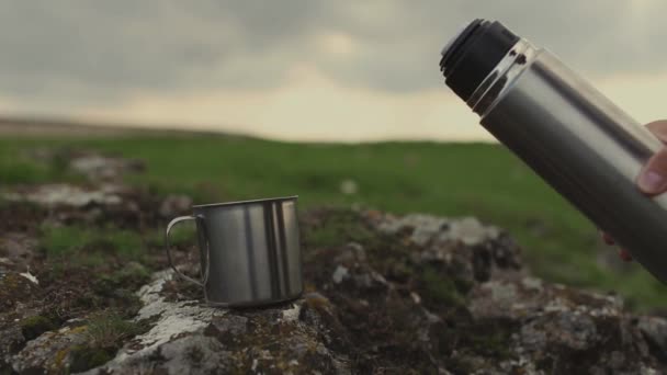 ハイキングの山の魔法瓶から暖かいお茶をスチールカップに注ぐ男性の手のクローズアップ — ストック動画