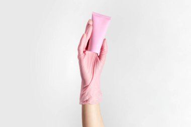 Kadın elinin eldiven giydiği yakın plan, beyaz stüdyo arka planında izole edilmiş, pastel mercan pembe renkli kozmetik tüp..