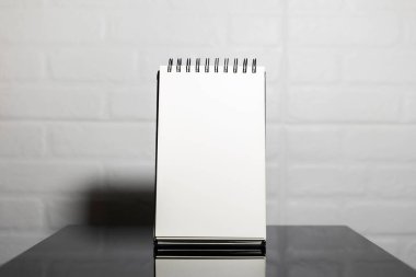 Siyah cam masadaki boş defter sayfasını kapat, beyaz tuğla duvarın arka planı.