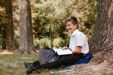 Bir ağacın altında bir parkta ödev yapan bir öğrenci.parkta bir ağacın altında oturan öğrenci