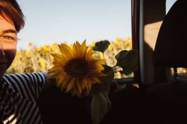 Ayçiçekleri ile alanında araba penceresinden görünümü. Adam sahadaki arabanın camından dışarı bakıyor.