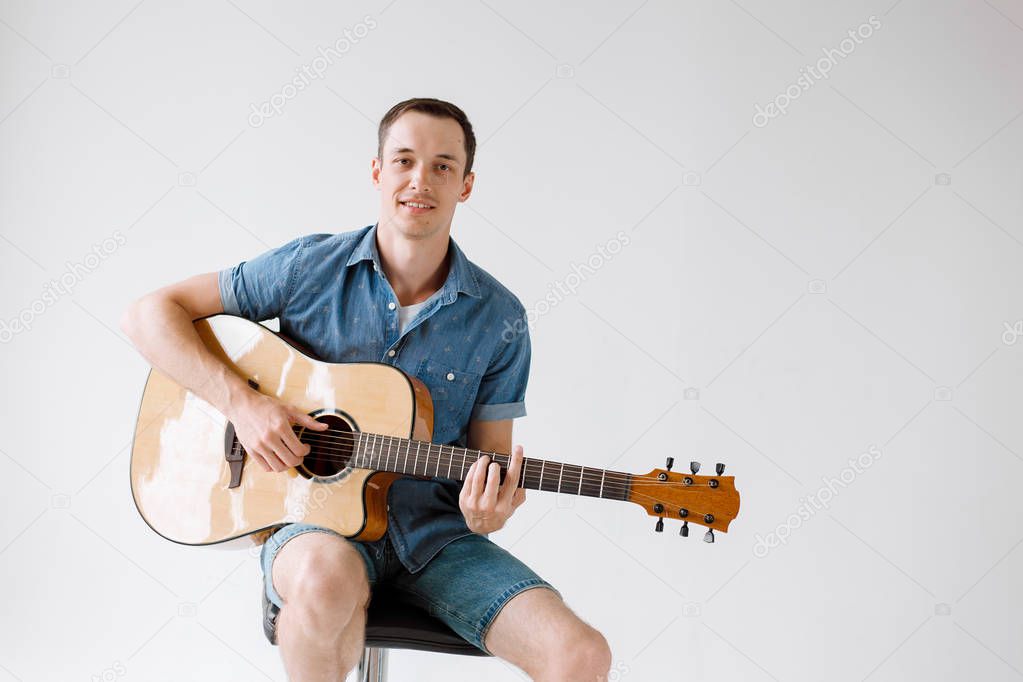 Handsome and cheerful guy musician in a shirt playing guitar