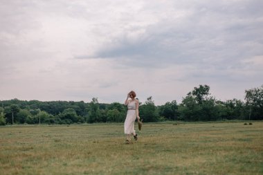 Kızıl saçlı kız güzel bir elbise ve şapka bir alanda yürüyüş