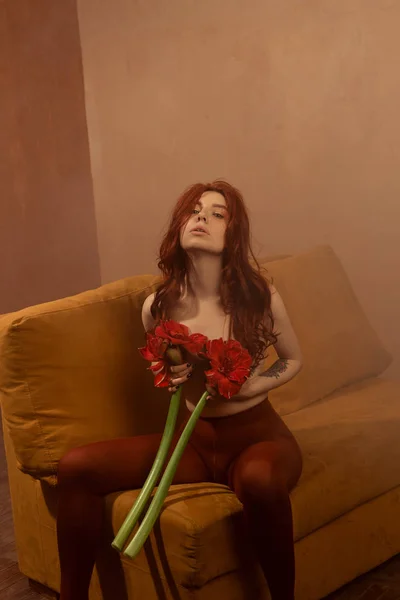 Beautiful girl with red hair, makeup and styling. Red flowers in the hands