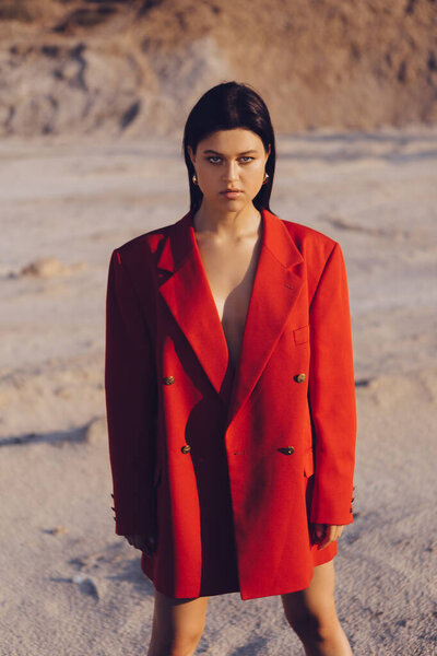 Stylish girl in fashionable clothes at sunset on the nature. Sand, lake and forest.