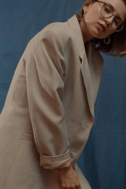 Gözlüklü güzel kız, mavi arka planda ceket ve kot pantolon.