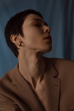 Kısa saçlı gözlüklü güzel kız, mavi arka planda bir ceket ve kot pantolon.