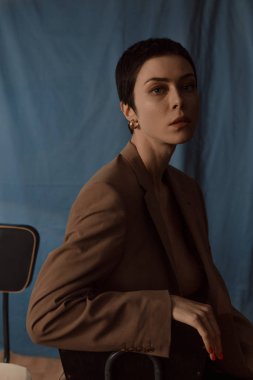 Kısa saçlı gözlüklü güzel kız, mavi arka planda bir ceket ve kot pantolon.