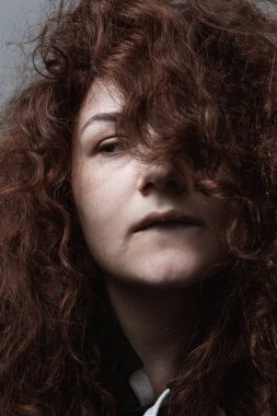 Gri arkaplanda kızıl saçlı güzel kıvırcık saçlı bir kızın portresi.
