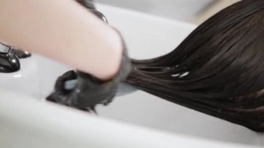Kuaför, bir güzellik salonunda uzun saçlı bir kızın kafasını yıkıyor.