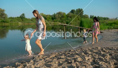 Suda çalışan mutlu neşeli çocuklar. İki genç güzel anne çocuk Nehri yakınında eğlenin. Yaz Gölü sabah güneşli gün mavi gökyüzü. Ağır çekim 30p 0,5 60 p