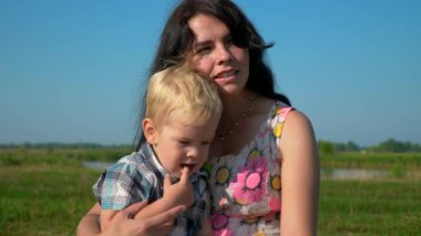 Mutlu genç sarılma ve öpüşme şirin çocuk ellerinde tutan anne. Yaz nehir Gölü sabah güneşli gün mavi gökyüzü. Ağır çekim 30p 0,5 60 p