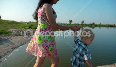  Anne ve oğlu yakınındaki nehre doğru yürüyüş. Çocuk işaret parmağı Nehri üzerinde. Yaz Gölü sabah güneşli gün mavi gökyüzü. Ağır çekim 30p 0,5 60 p