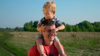 Genç yakışıklı tatlı çocuk omuzlarında taşıyan Baba adam. Yaz sabahı güneşli bir gün mavi Clea gökyüzü kırsal yol. Yavaş hareket 30 p 0,5 60 p