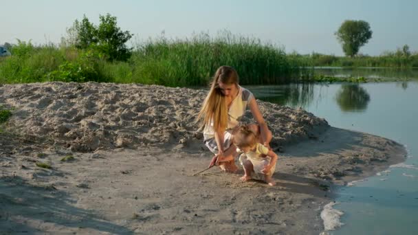 若い子と美しい母をプレイ 川湖の近くの砂の上を描画します 夏の朝晴れた青い空 スローモーション — ストック動画