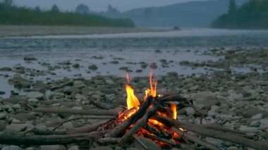 Kayalık nehir kıyısında kamp ateşi. Orman arka plan yakınındaki Mountians akşamları