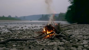 Kayalık nehir kıyısında kamp ateşi. Orman arka plan yakınındaki Mountians akşamları