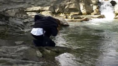 Geniş atış. Adam içme suyu dağ nehir. Siyah pelerin Hood baca şapkası ile. Yaz güneşli gün. 4 k yavaş hareket