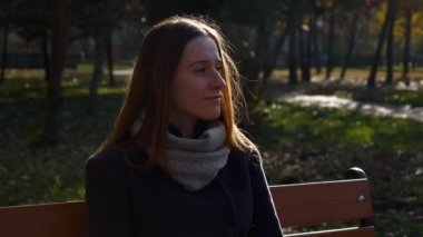 Bir tarihleme için bekleyen parkta bankta oturmuş 4 k 60 p güzel bir kız. Sonbahar güneşli gün