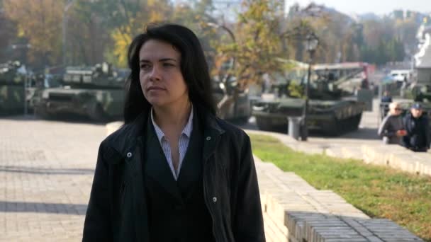 美丽的迷人的女孩走和思考 背景下城市广场上的军车 慢动作 2019年乌克兰基辅 — 图库视频影像