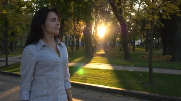 自信を持って美しい成功した女性は 都市公園と思考で歩きます 夕方日没の背景 都市公園における秋の晴れた日 レンズ フレア スローモーション Fps — ストック動画