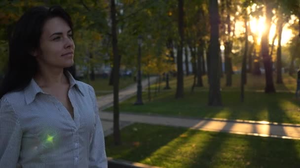 自信美丽的成功女子走在城市公园和思考 晚上的日落背景 城市公园里的秋日 镜头耀斑 慢动作 — 图库视频影像