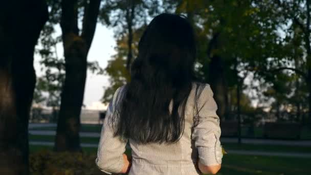 美丽的女孩把叶子握在手里 转身躲在树叶后面 快乐的积极情绪 晚上黄金时间在公园里 慢动作 Fps — 图库视频影像