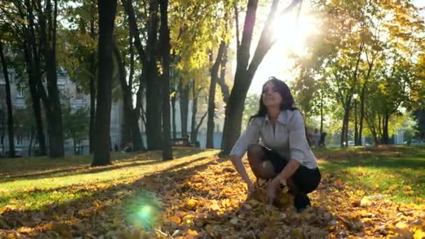 快乐的女孩在空中扔黄叶 下降慢动作 美丽的夜晚阳光在城市公园 镜头闪光灯 — 图库视频影像