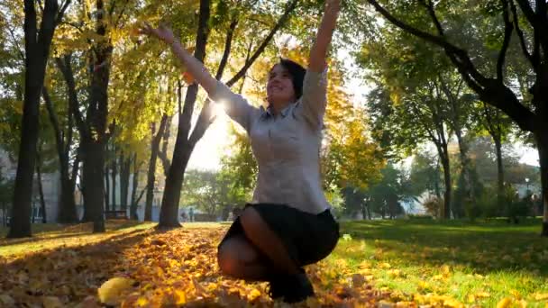 幸せな少女は 空気で黄色の葉をスローします 落ちるスローモーション 都市公園における美しい夜のサンシャイン レンズ フレア — ストック動画