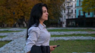 İş kadını akıllı telefon kullanarak sokakta yürüyor. Çalışma günü işe sonra Shift rahatlatıcı dinleniyor. Smartphone'da sohbet. Akşam şehir şehir. 4k yavaş hareket 60 fps