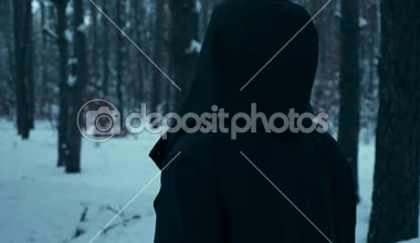 Siyah pelerin yürüyüş Hood ile Ortaçağ adam. Akşam alacakaranlık Twilight. Kış ormanda seyahat avare. Kar ağaçlar ahşap kaplı