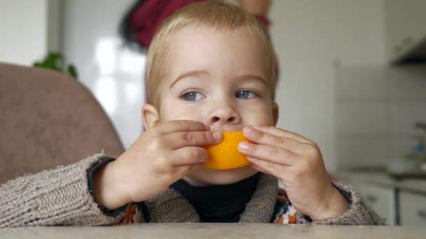 Ładny Mały Chłopiec Zjada Smaczny Orange Kuchni Niewyraźne Tło Rodziców — Wideo stockowe