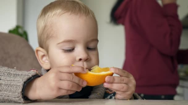 Cute Little Boy Eats Tasty Orange Kitchen Blurred Background Parents — Stock Video