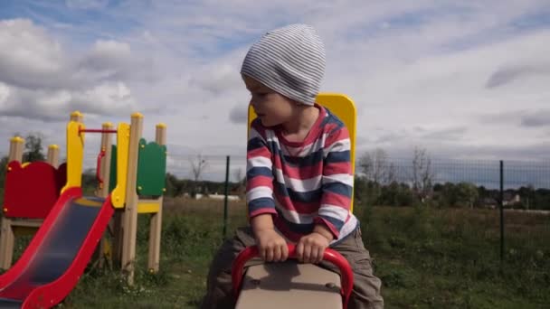 Fröhlich Fröhlicher Kleiner Junge Schaukelt Auf Schaukelspielen Auf Dem Kinderspielplatz — Stockvideo