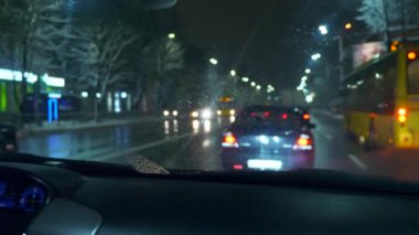 Gece sürüş. Şehir cadde boyunca hareketli araba açık görünümden ıslak ön cam üzerinde çalışan silecekler. Bulanık araçlar kentsel yolda. Kış akşam kar yağışı yavaş hareket 0,5 hızı 50fps