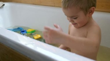 Mutlu neşeli çocuk oyuncakları küvet suda ile gülümseyen çalış. Sevimli küçük çocuk banyoda eğleniyor. Ağır çekim 0,5 hızı 60fps