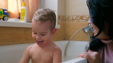 Mutlu neşeli çocuk küvet banyo genç güzel annesi ile oynayan ve su sıçramalarına yapar. Ağır çekim 0,5 hız 60 fps