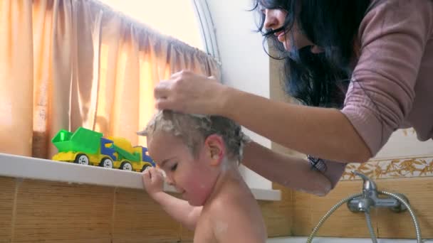 年轻母亲的手洗孩子的头发和头部在浴室里 照顾可爱的儿子 快乐的孩子沐浴在浴室的浴缸里 — 图库视频影像