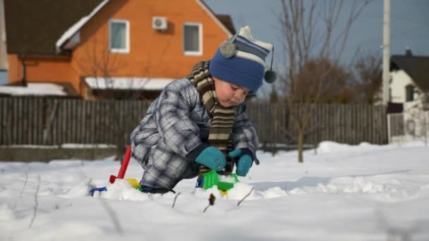 少年は裏庭の庭で雪でオモチャのトラックで果たしています 年末年始の寒さ 明るく晴れた日 Fps スローモーション — ストック動画