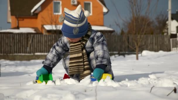 少年は裏庭の庭で雪でオモチャのトラックで果たしています 年末年始の寒さ 明るく晴れた日 Fps スローモーション — ストック動画