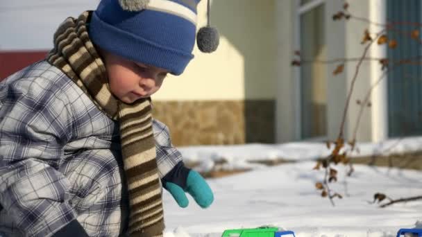 少年は裏庭の庭で雪でオモチャのトラックで果たしています 年末年始の寒さ 明るく晴れた日 Fps スローモーション — ストック動画
